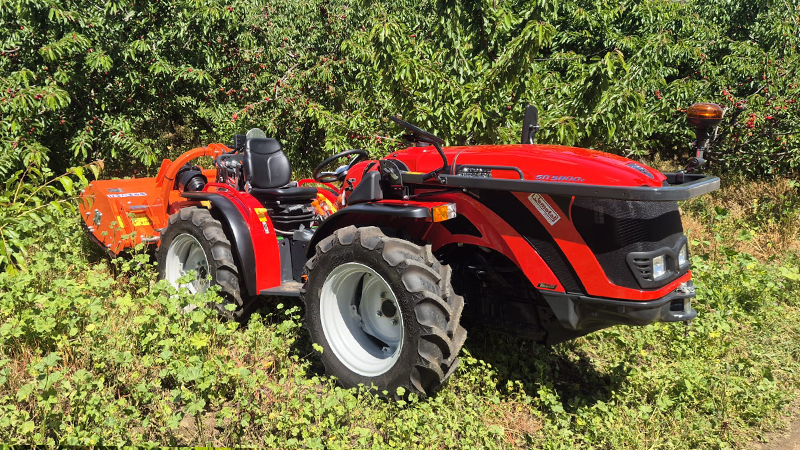 Tractor agrícola articulado Antonio Carraro SN 5800 V de color rojo trabajando con apero en una plantación de frutales.